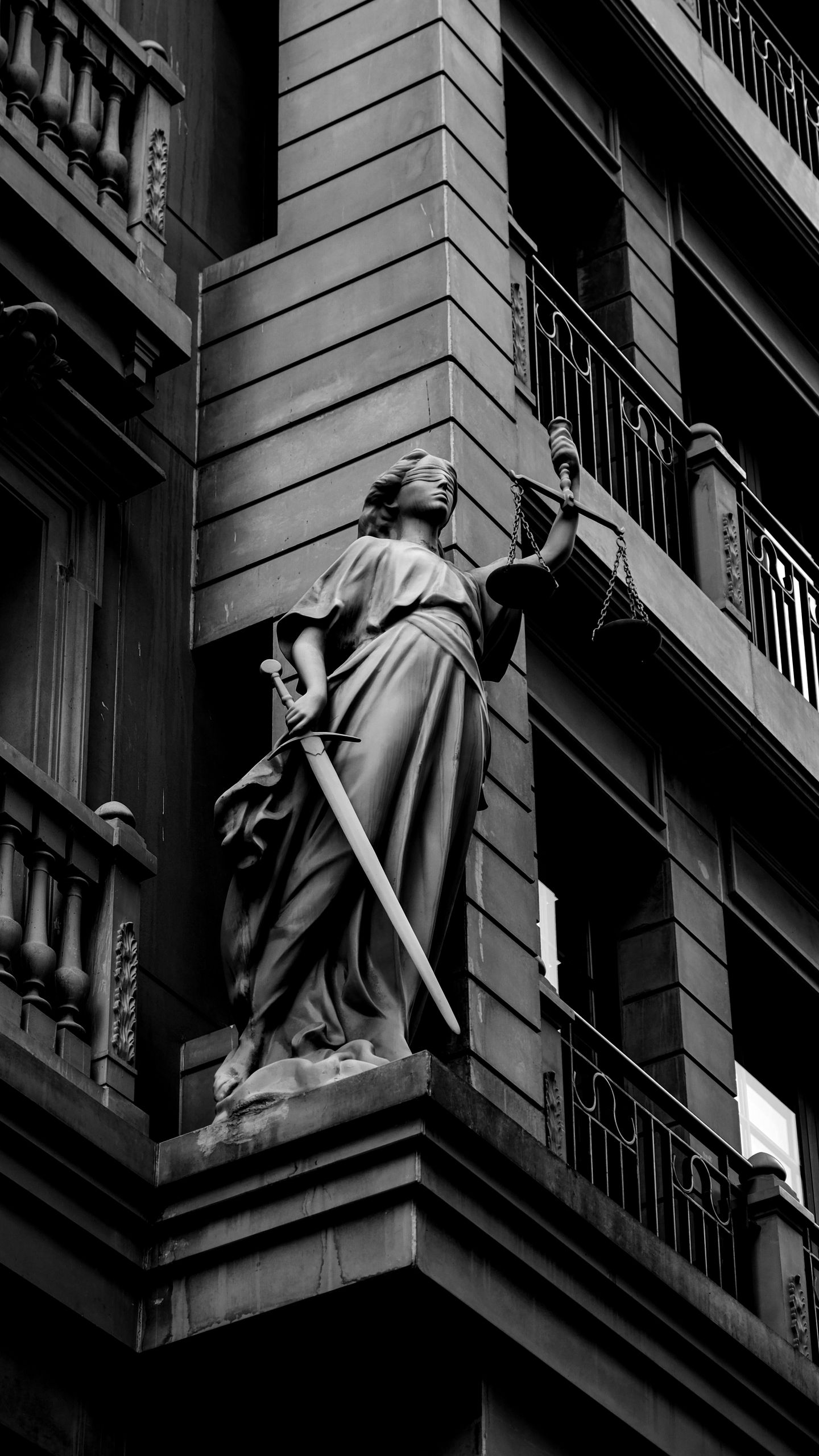 A dramatic black and white photo of a justice statue holding a sword and scales.